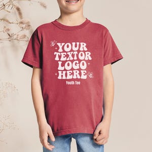 May include: A red youth tee shirt with the text "YOUR TEXTOR LOGO HERE" in white, with butterfly graphics. The shirt is worn by a person wearing blue jeans.