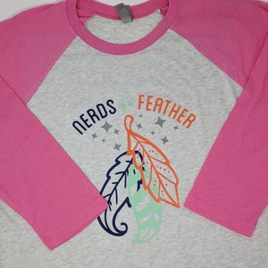 May include: A gray and pink baseball tee shirt with a graphic of two leaves and the text "NERDS of the FEATHER".