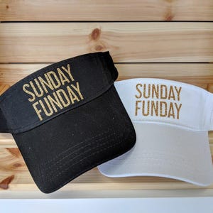 May include: Two black and white visors with gold glitter lettering. The black visor says "SUNDAY FUNDAY" and the white visor says "SUNDAY FUNDAY".