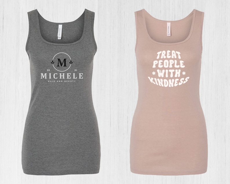 May include: Two tank tops, one gray with a white logo that says "Michele Hair and Beauty" with a stylized "M" and the numbers "20" and "21" on either side of the "M", and the other a light pink tank top with the text "Treat People With Kindness" in white.