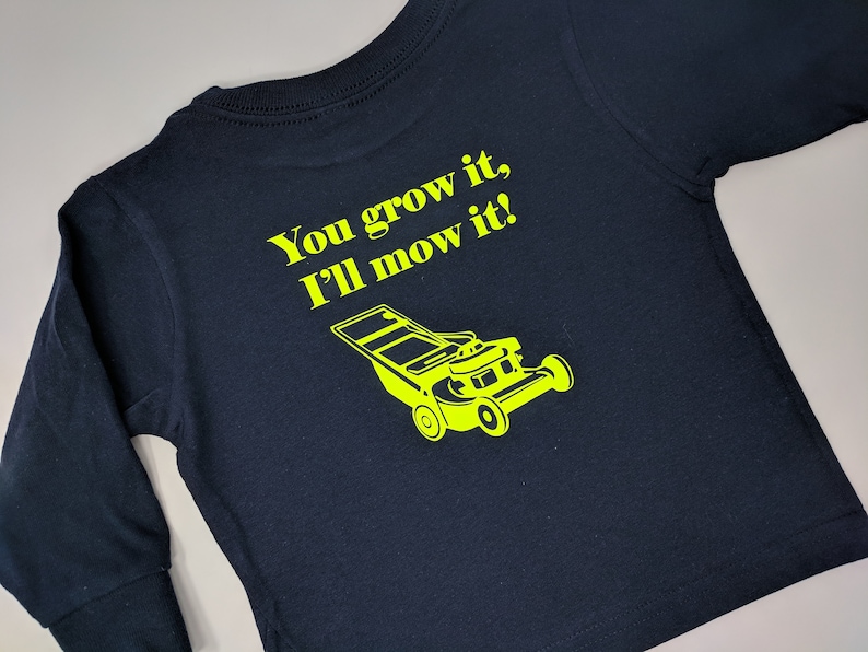 May include: A navy blue long-sleeved shirt with the text "You grow it, I'll mow it!" in yellow lettering. A yellow silhouette of a lawnmower is below the text.