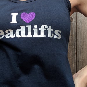 May include: A black tank top with a silver glitter design that says "I heart Deadlifts" with a purple glitter heart.