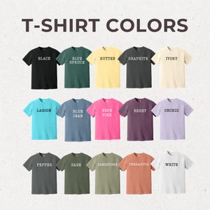 May include: A chart of 15 different t-shirt colors, each color is represented by a t-shirt with the color name printed on it in white text. The colors are: Black, Blue Spruce, Butter, Graphite, Ivory, Lagoon, Blue Jean, Neon Pink, Berry, Orchid, Pepper, Sage, Sandstone, Terracotta, and White.