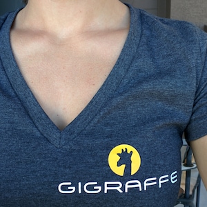 May include: A dark grey V-neck t-shirt with a white logo that says "GIGRAFFE" and a yellow circle with a silhouette of a giraffe's head.