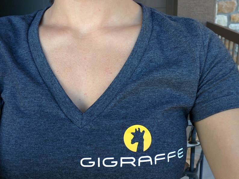 May include: A dark grey V-neck t-shirt with a white logo that says "GIGRAFFE" and a yellow circle with a silhouette of a giraffe's head.