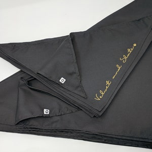 May include: A stack of black bandana dog bandanas with gold embroidery that reads "Velvet and Slate".