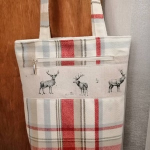 Puede incluir: Una bolsa de mano de cuadros rojos y blancos con un bolsillo con cremallera y un dise&ntilde;o de estampado de ciervos. La bolsa tiene dos asas.