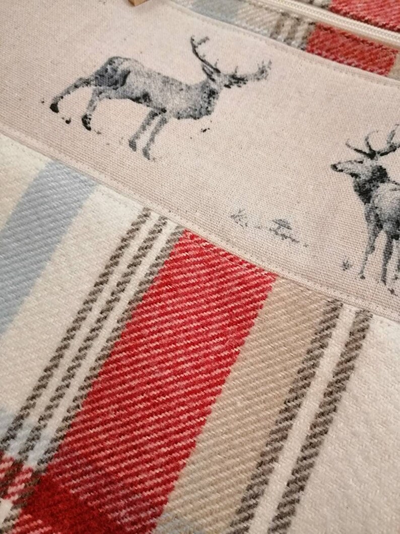 Puede incluir: Primer plano de una tela con un patr&oacute;n de cuadros rojos, blancos y grises. La tela tiene un dise&ntilde;o impreso de dos ciervos, uno con cuernos y otro sin.