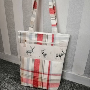 Puede incluir: Una bolsa de mano de cuadros rojos y blancos con cierre de cremallera y un dise&ntilde;o de estampado de ciervo. La bolsa tiene dos asas.