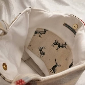 Puede incluir: Una bolsa de tela blanca con un patr&oacute;n de cuadros rojos y azules. La bolsa tiene un forro blanco con un estampado de ciervos y una etiqueta que dice "Hand Made in Scotland by Handmade Scotland".