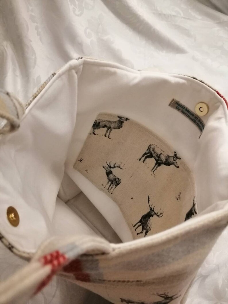 Puede incluir: Una bolsa de tela blanca con un patr&oacute;n de cuadros rojos y azules. La bolsa tiene un forro blanco con un estampado de ciervos y una etiqueta que dice "Hand Made in Scotland by Handmade Scotland".