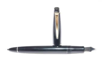 May include: Black fountain pen with a gold-colored clip and accents. The pen is lying horizontally with the cap standing upright. The nib is visible, and the pen has a sleek, classic design.