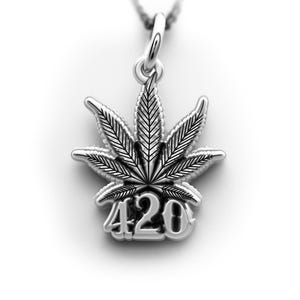 May include: Silver-toned pendant necklace featuring a detailed cannabis leaf design with the number "420" at the base. The pendant is suspended from a delicate chain, creating a simple yet eye-catching accessory.