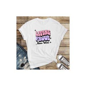 May include: White t-shirt with a pink and purple graphic that says "Living Proof" with the words "Chaos Works" underneath.