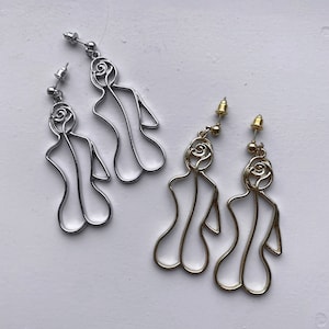 Puede incluir: Un par de pendientes de plata y oro con una figura femenina estilizada con un diseño de rosa. Los pendientes son de estilo colgante y tienen un cierre de poste.