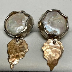 May include: A pair of silver and gold earrings with a large, white pearl in the center of each earring. The pearl is surrounded by a silver setting, and the earring is attached to a gold, hammered drop.