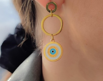 May include: Gold-toned drop earrings featuring a circular design with a smaller circle at the top, a larger circle in the middle, and a round pendant at the bottom. The pendant has a white background with a blue eye design.