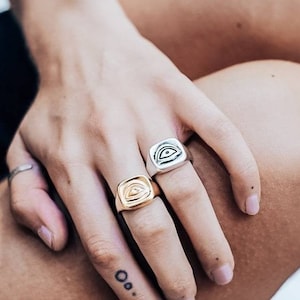 Pu&ograve; includere: Due anelli a sigillo quadrati con un designo a forma di occhio. Un anello &egrave; d'argento e l'altro &egrave; d'oro.