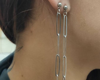 May include: Silver-toned chain link earrings. Each earring features a small ball stud at the top, with a series of elongated oval links cascading downwards. The earrings are designed to dangle, creating a sleek, modern look.