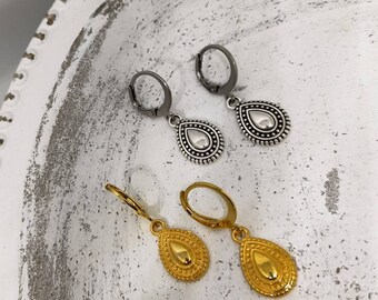 May include: Two pairs of teardrop earrings. One pair is silver-toned with a beaded border and a lever back closure. The other pair is gold-toned with a similar design. The earrings are displayed on a white, textured surface.