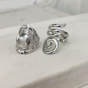 May include: Two silver rings, one with a round, textured design and the other with a spiral design.