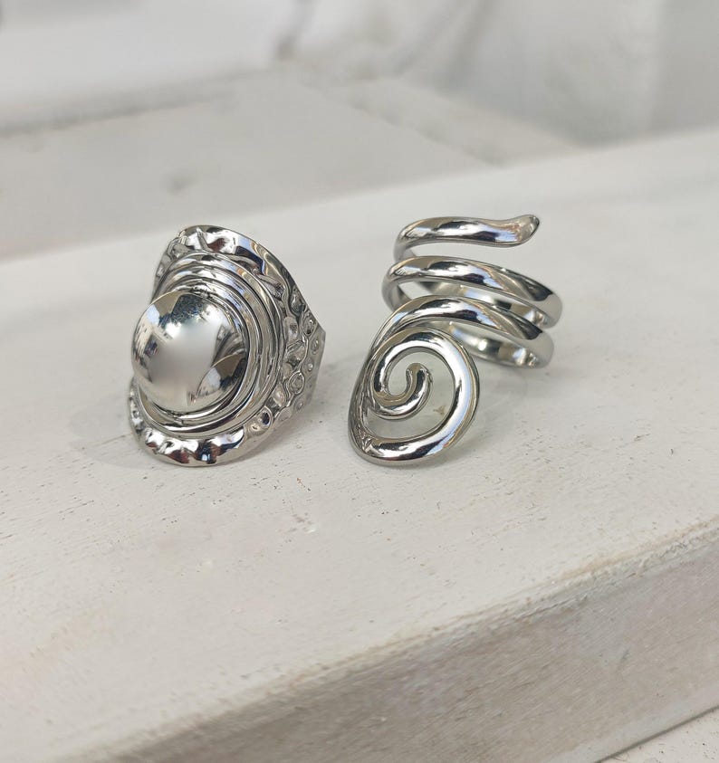 May include: Two silver rings, one with a round, textured design and the other with a spiral design.