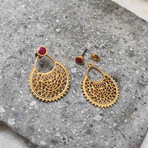 Puede incluir: Pendientes de filigrana dorados con un acento de piedra preciosa roja. Los pendientes presentan un diseño circular con intrincados patrones y una forma de lágrima. También hay un pendiente de botón y un cierre a juego.