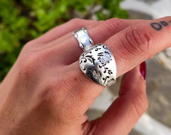 May include: A silver ring with a floral design. The ring is worn on a finger.