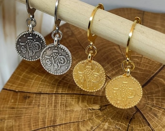 May include: Four hoop earrings with coin-shaped charms. Two earrings have silver charms with an intricate design and two earrings have gold charms with an intricate design.