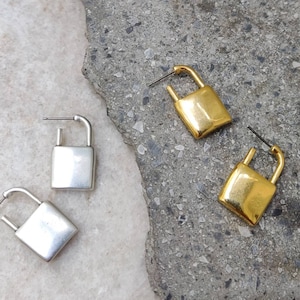 Peut inclure: Une paire de boucles d'oreilles en forme de cadenas, l'une en argent et l'autre en or. Les boucles d'oreilles sont simples et élégantes, et feraient un excellent cadeau pour un ami ou un être cher.