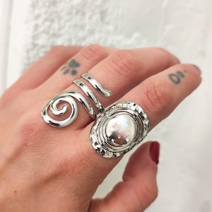 Op de afbeelding: Twee zilveren ringen, een met een spiraalvormig ontwerp en de andere met een rond, gehamerd, getextureerd oppervlak.