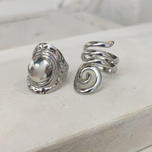 May include: Two silver rings, one with a round, textured design and the other with a spiral design.