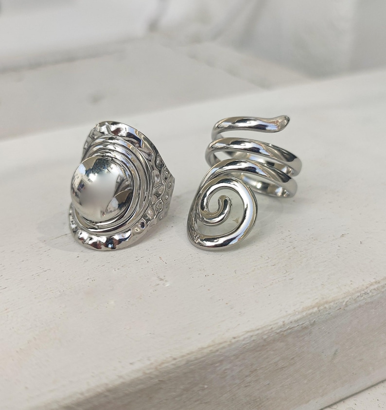 May include: Two silver rings, one with a round, textured design and the other with a spiral design.