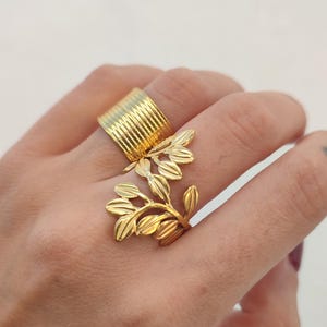 Può includere: Due anelli d'oro, uno con una fascia testurizzata e l'altro con un design a foglia.