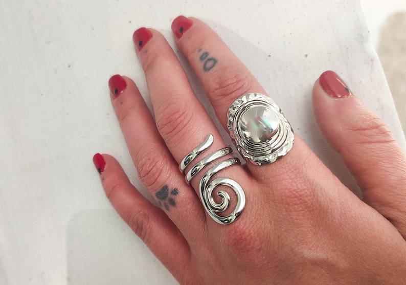 May include: Two silver rings on a hand. One ring is a spiral design and the other is a round ring with a raised center.