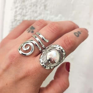 May include: Two silver rings on a finger. One ring is a spiral design and the other is a round ring with a hammered texture.