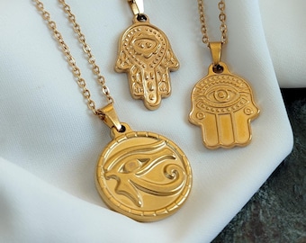 May include: Three gold-toned necklaces featuring distinct pendants. One pendant is a circular disc with an Eye of Horus design, while the other two are Hamsa hand-shaped charms, each displaying an eye motif within the palm area.