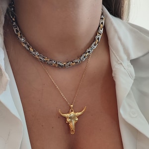 May include: A gold bull skull pendant necklace on a gold chain layered over a silver and gold chain necklace.