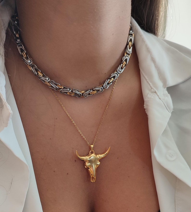 May include: A gold bull skull pendant necklace on a gold chain layered over a silver and gold chain necklace.