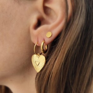 Puede incluir: Juego de pendientes dorados. El conjunto incluye un par de pendientes de aro con colgantes en forma de coraz&oacute;n, un par de pendientes de aro peque&ntilde;os y un par de pendientes de bot&oacute;n redondos. Los colgantes de coraz&oacute;n tienen una superficie texturizada.