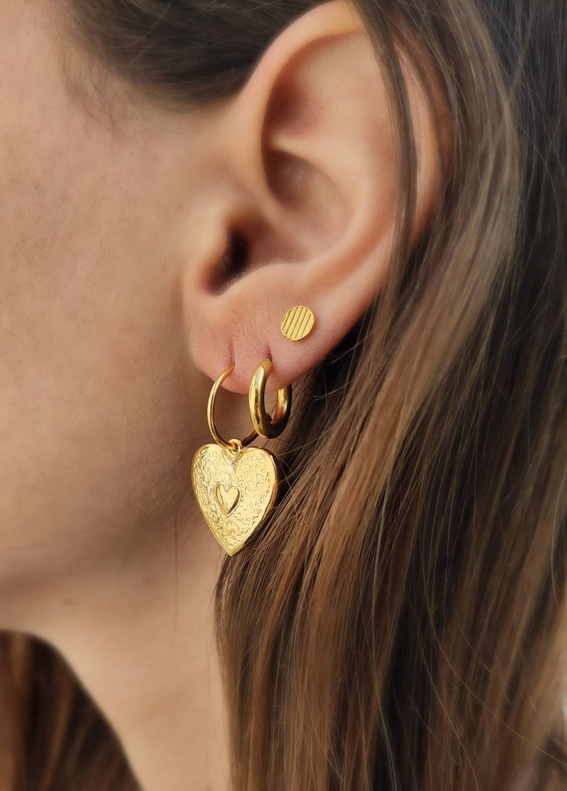 Puede incluir: Juego de pendientes dorados. El conjunto incluye un par de pendientes de aro con colgantes en forma de coraz&oacute;n, un par de pendientes de aro peque&ntilde;os y un par de pendientes de bot&oacute;n redondos. Los colgantes de coraz&oacute;n tienen una superficie texturizada.