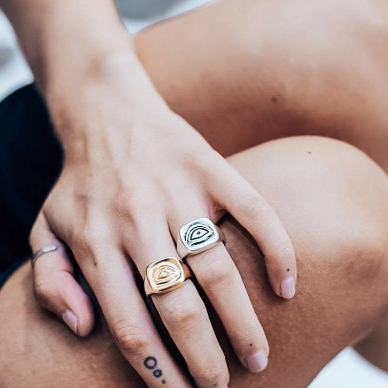 Pu&ograve; includere: Due anelli a sigillo quadrati con un designo a forma di occhio. Un anello &egrave; d'argento e l'altro &egrave; d'oro.