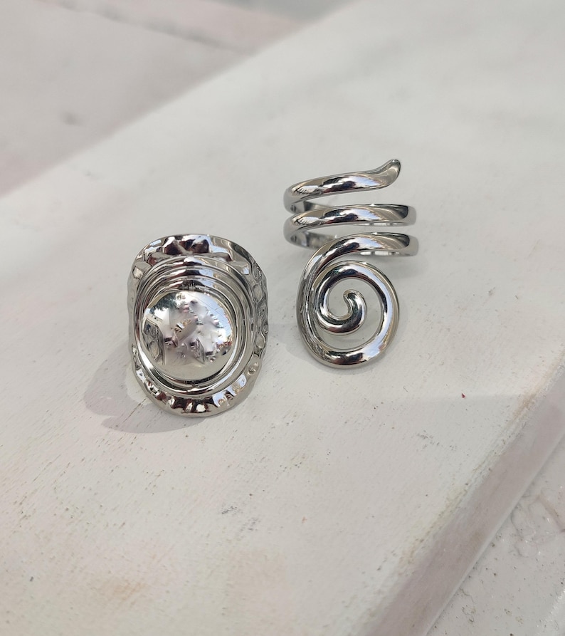 May include: Two silver rings. One ring has a textured, circular design. The other ring is a spiral.