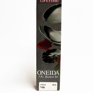 May include: A box for a 3-piece Oneida Volta Hostess Set, made of 18/10 LTO stainless steel. The box is black with a silver spoon and the Oneida logo. The text "Flatware For A LIFETIME" is printed on the box.