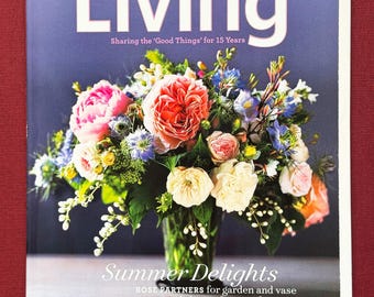 Può includere: La copertina della rivista Martha Stewart Living presenta una vivace composizione floreale in un vaso trasparente. Il bouquet include fiori rosa, arancioni, bianchi e blu. Il titolo della rivista "Living" è ben visibile, con il testo "Summer Delights" sotto.