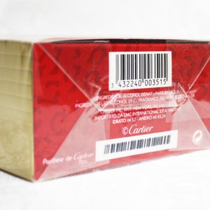 Pu&ograve; includere: Una scatola rossa e dorata con un codice a barre e il testo "Cartier" sul lato. La scatola &egrave; avvolta in plastica trasparente.