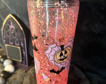 May include: Pink glitter tumbler with a black rim and a Halloween design featuring bats, a spiderweb, and a pumpkin.
