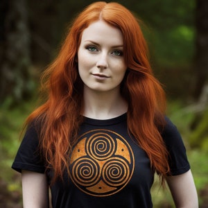 May include: A woman with long, red hair wearing a black t-shirt with a gold, three-spiral design on the front.