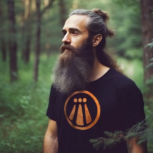 May include: A man with a long grey beard and hair pulled back in a bun is wearing a black t-shirt with an orange symbol on the front. The symbol is a circle with three vertical lines inside. The man is standing in a forest.
