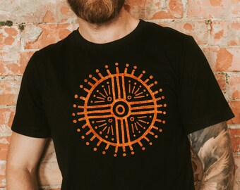 May include: A black t-shirt featuring an orange geometric design on the front. The design is a circle with a cross inside, and it has a sunburst pattern around the edges.